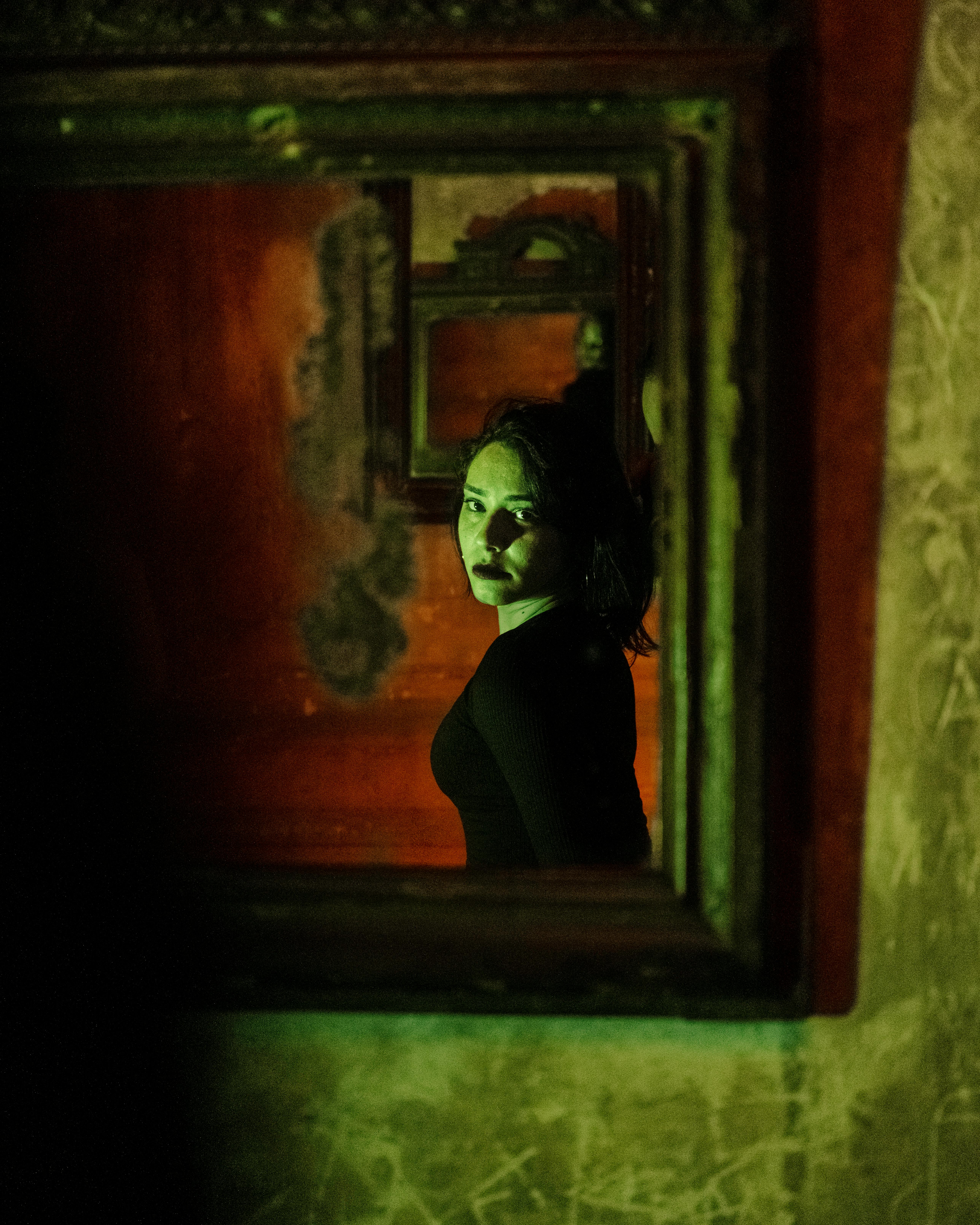 A mysterious woman in dim light reflects multiple times through a vintage mirror.