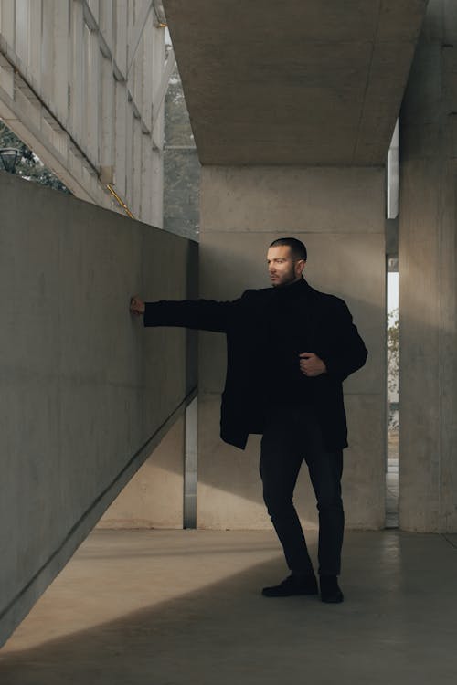 A man in a black coat standing in front of a concrete wall