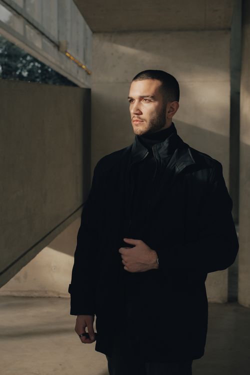 Free A well-dressed man in black clothing standing in a shadowy indoor setting. Stock Photo