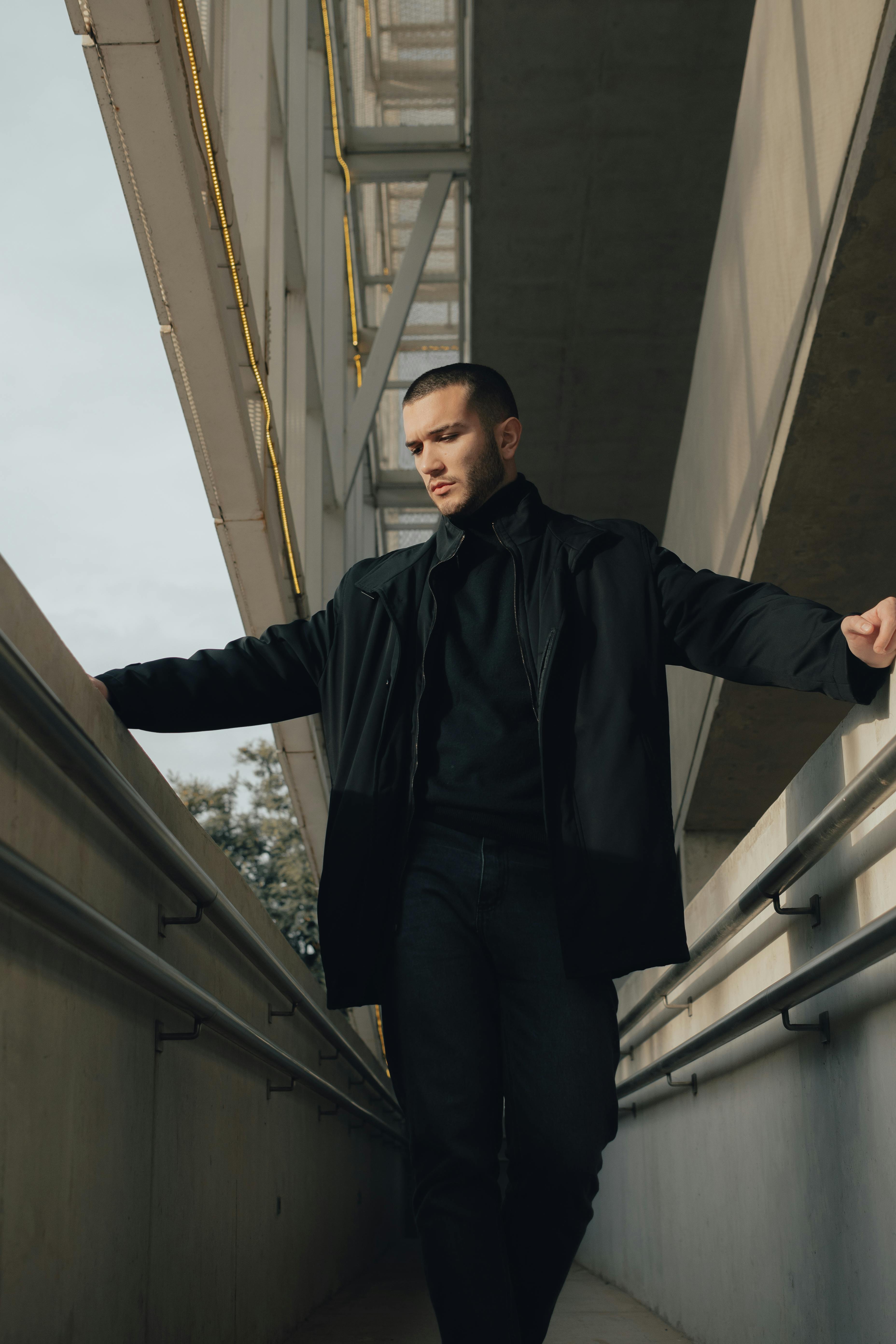 Stylish man in black coat posing under modern architecture in city.