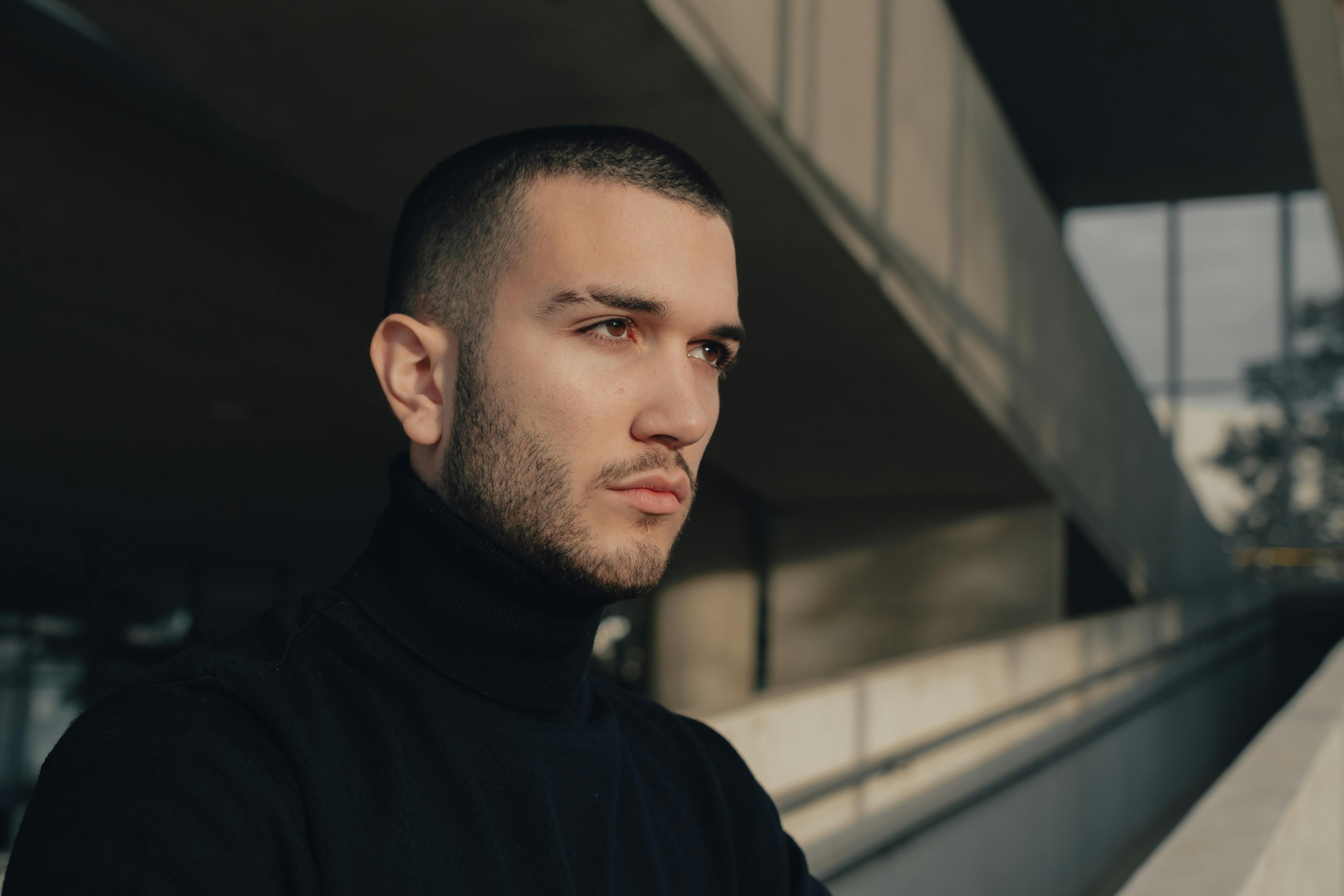 Profile shot of a thoughtful man in a black turtleneck, urban setting.