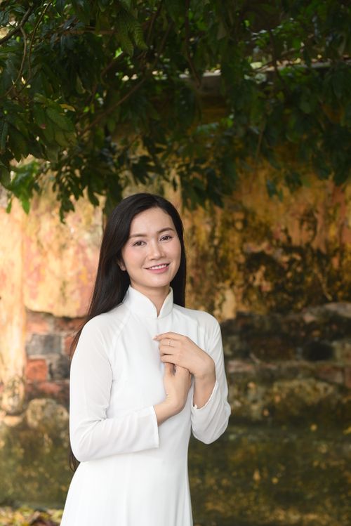 Free Portrait of an East Asian woman in a white Ao Dai standing outdoors, smiling warmly. Stock Photo