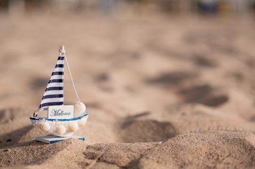 Free A small striped sailboat toy placed on sandy beach with soft focus background. Stock Photo