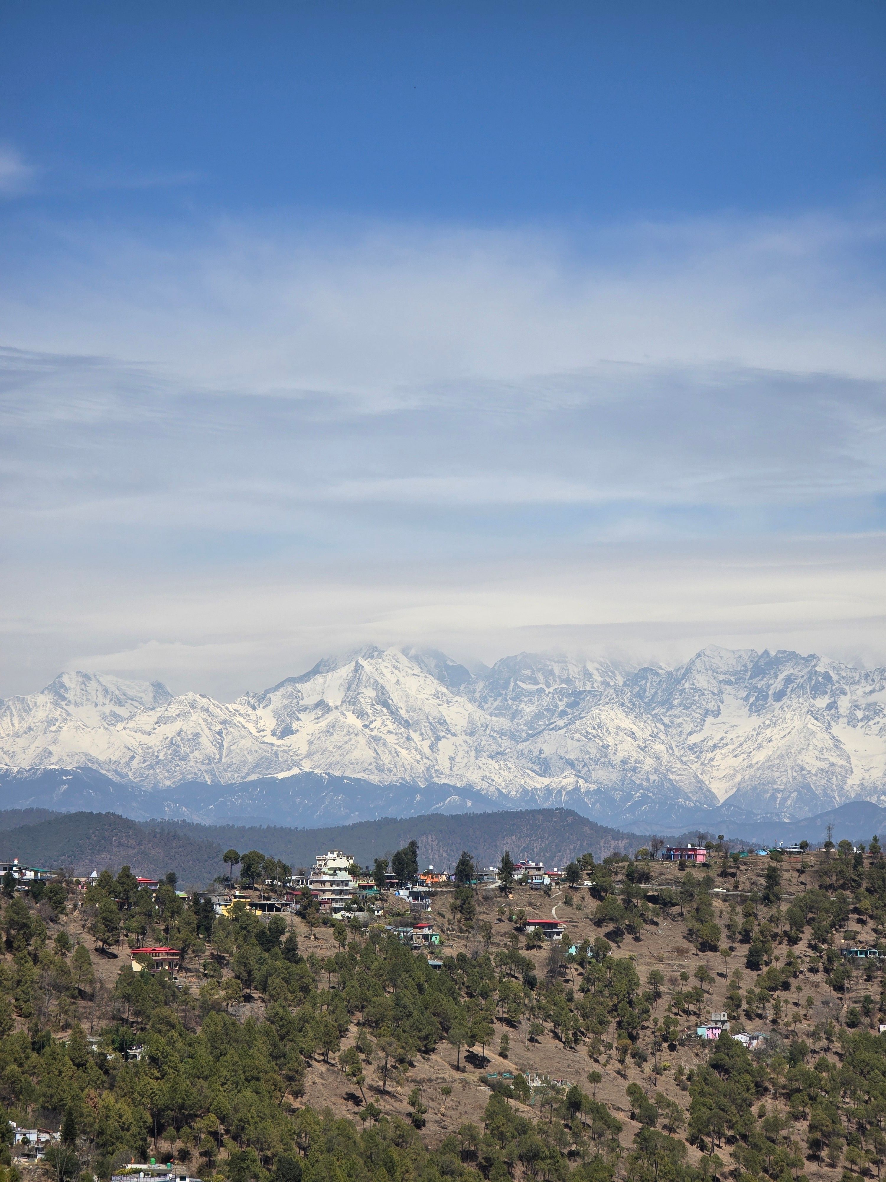 Picturesque view of the Himalayas with a charming Indian hill town in the foreground under a bright blue sky.
