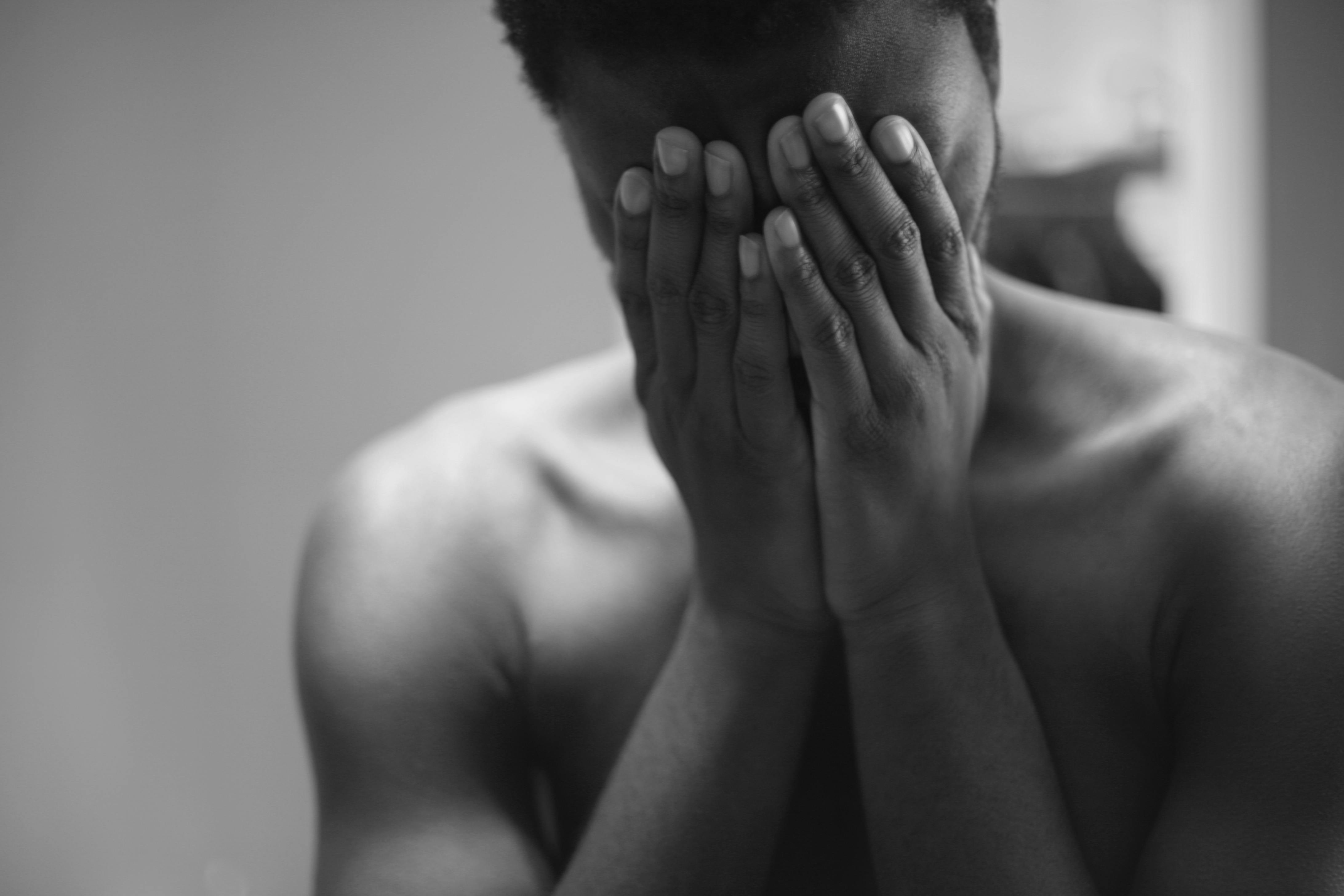 gray scale photo of topless man covering face