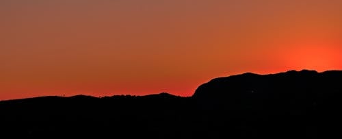 бесплатная Черная гора под коричневым небом во время заката Стоковое фото