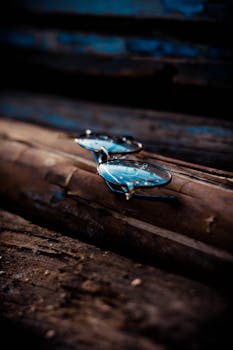 An artistic shot of eyeglasses with water droplets resting on aged wood, creating a moody atmosphere.