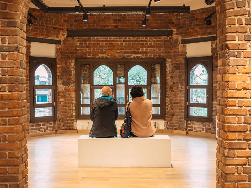 Two seniors admire museum architecture, seated on bench beneath brick arches - senior center history outings