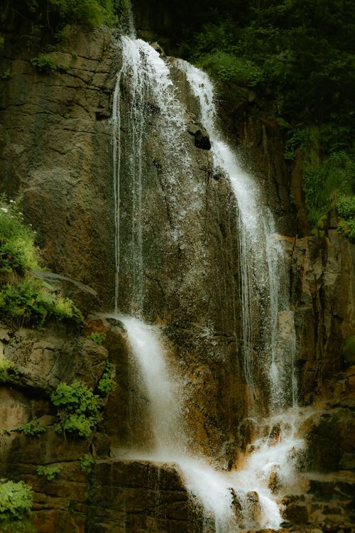 Free Majestic waterfall cascading down rocky cliffs surrounded by lush greenery in a serene forest setting. Stock Photo