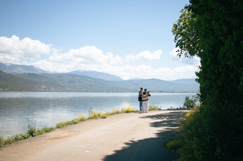 A couple is standing on the side of a road near the water