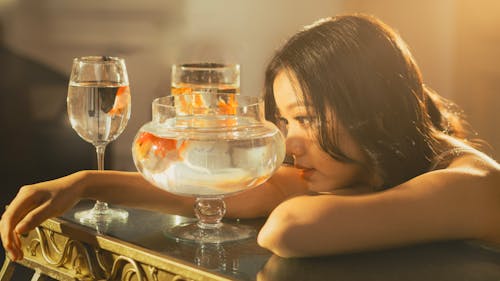 A woman is looking at a fish bowl with a glass of water