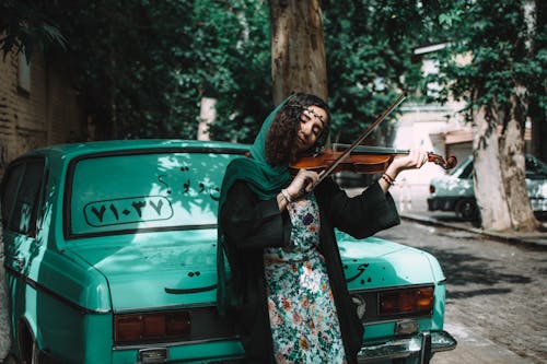 Free Woman Playing Violin While Leaning On Green Vehicle Stock Photo