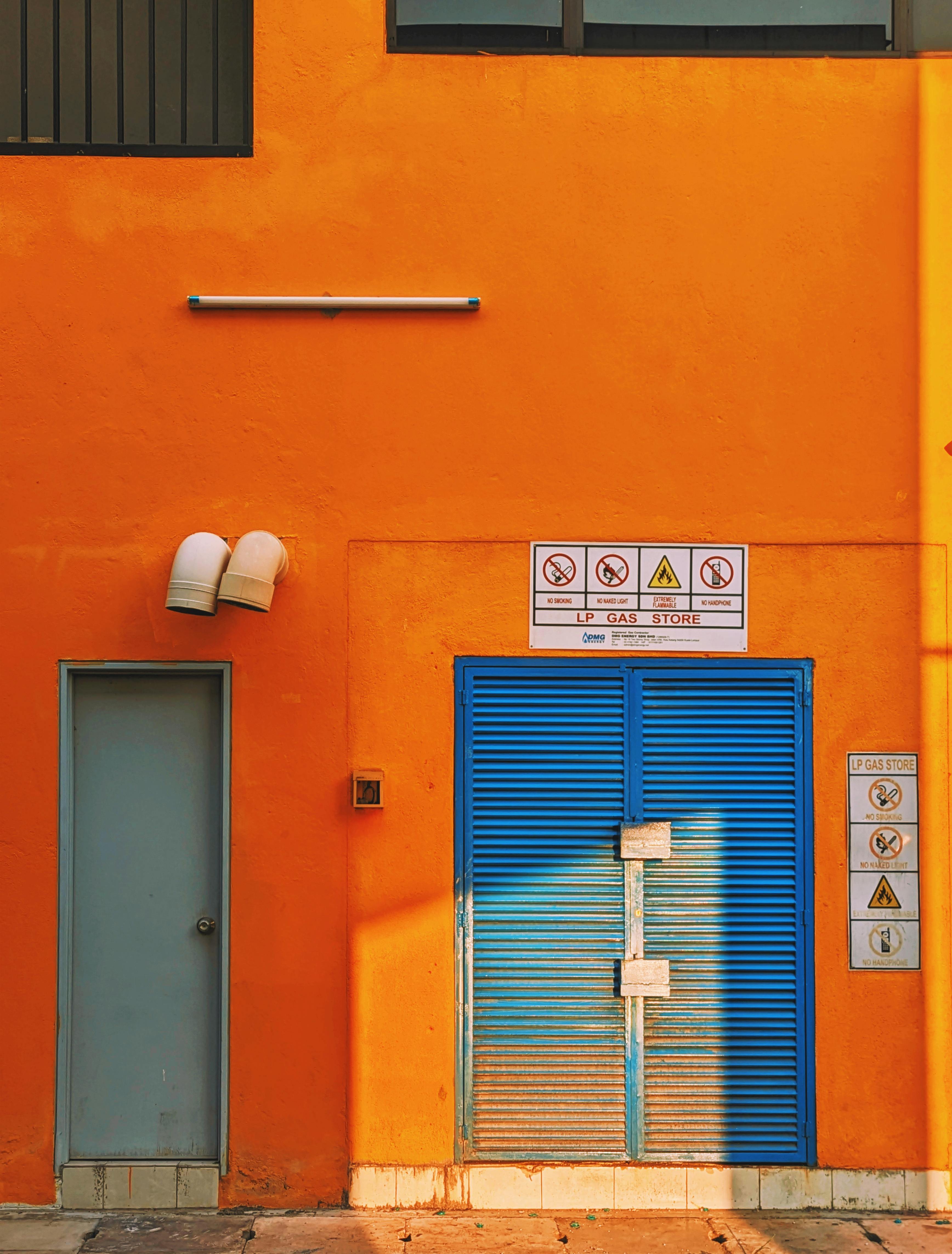 Vivid orange wall featuring blue doors and industrial warning signs, providing a bold urban aesthetic.