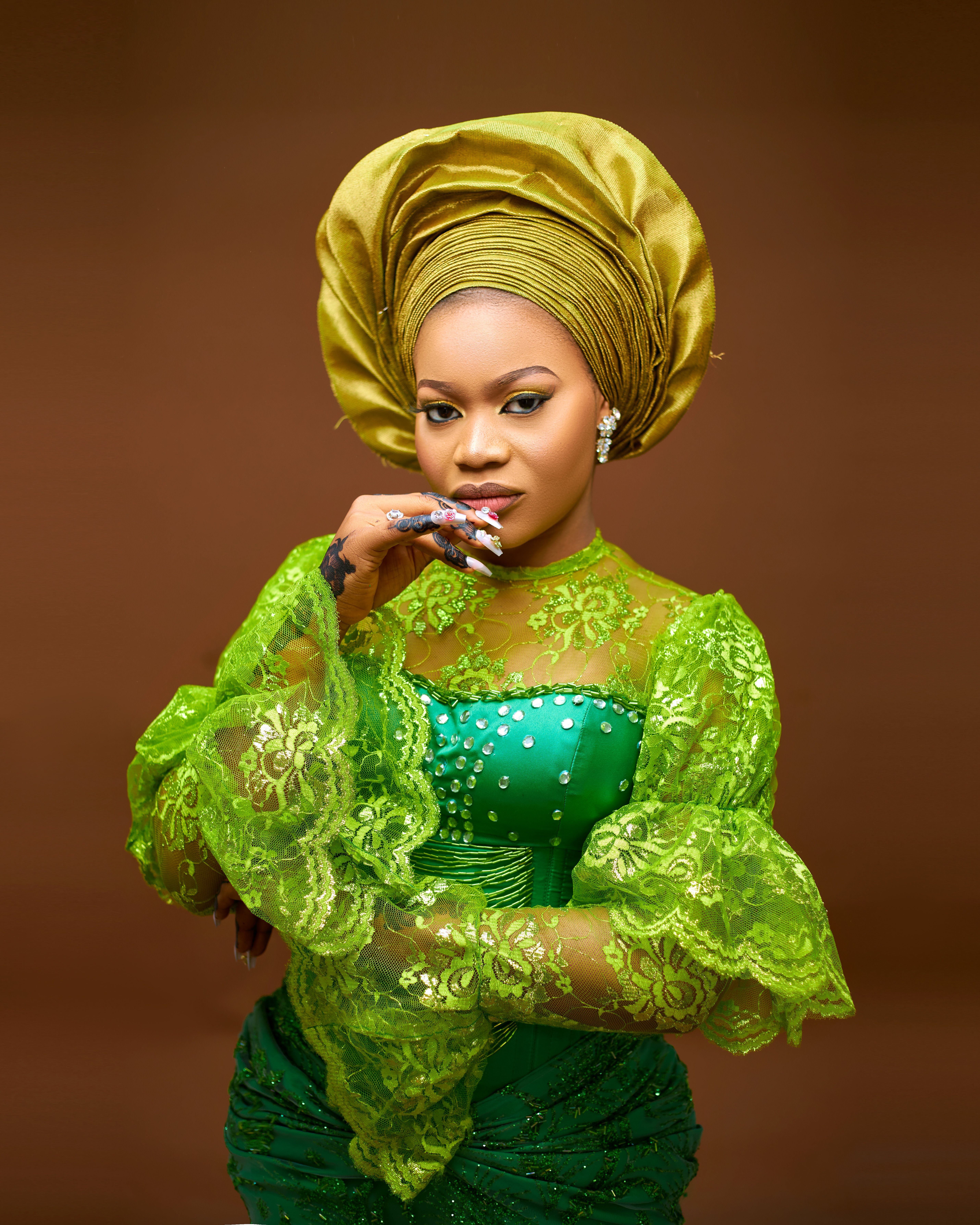 Stunning fashion portrait of a woman in a green dress and matching headwrap, set against a brown background.