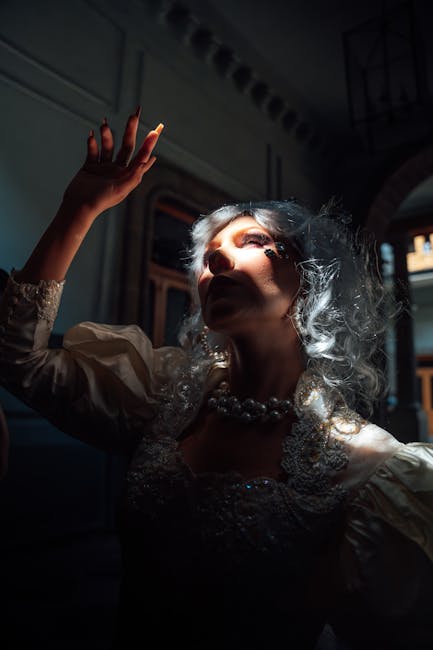 Elegant woman with white hair poses dramatically in shadow, highlighting a theatrical costume.