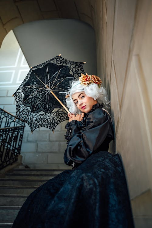Woman in Wig and Dress Standing with Umbrella on Stairs