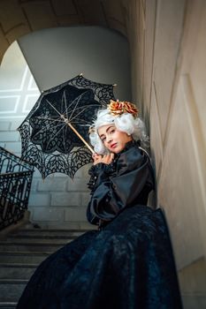 A sophisticated woman with white hair and a lace umbrella poses gracefully on stairs in an urban setting.