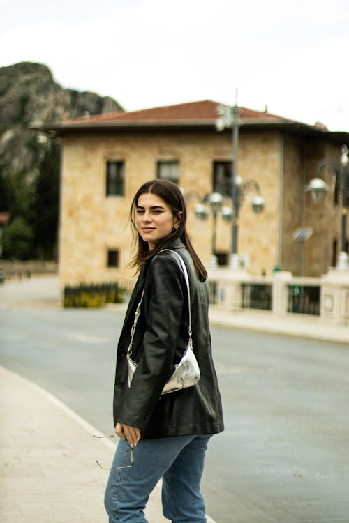 A woman in jeans and a leather jacket standing on a street