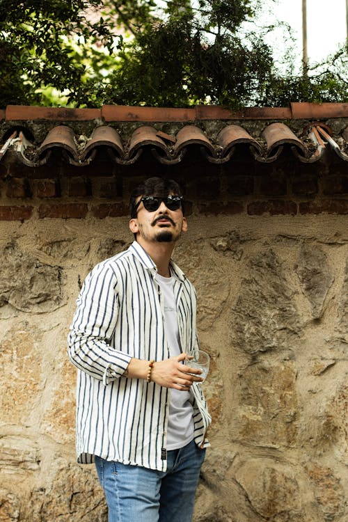 A man in sunglasses and striped shirt standing next to a wall