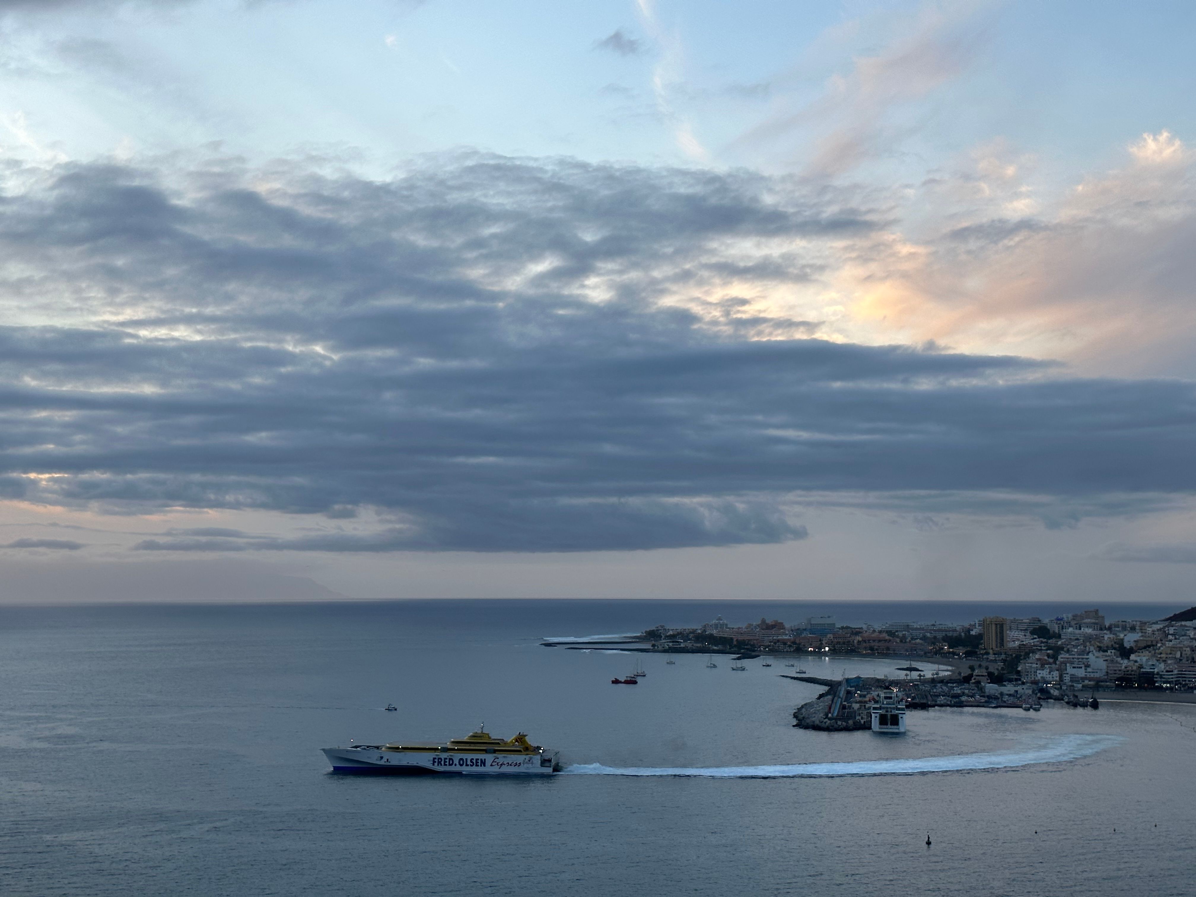 Panoramic aerial view of Los Cristianos Harbor with ferry at twilight under dramatic cloudscape.