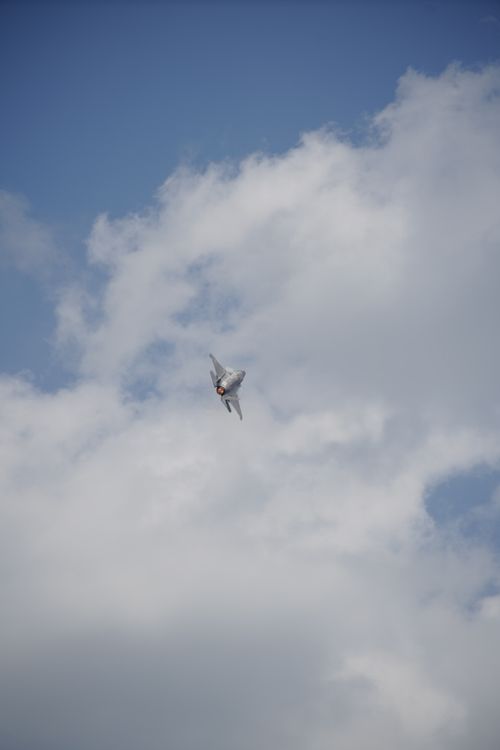 Free A fighter jet soars through a cloudy sky, exhibiting agile maneuvers against a backdrop of blue and white. Stock Photo