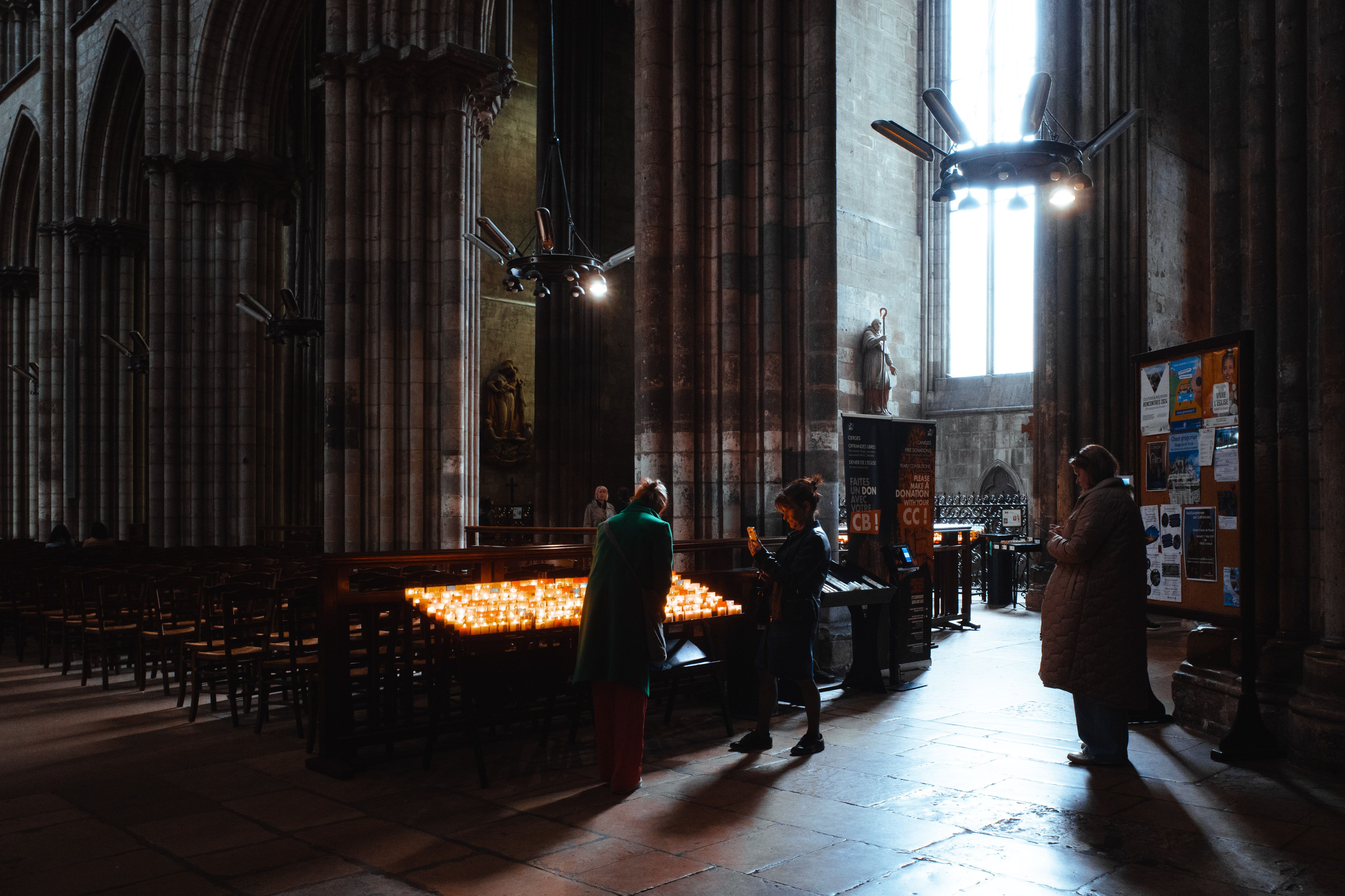 A person kneeling on a stone floor in a dark church, hands open, soft light from a stained glass window