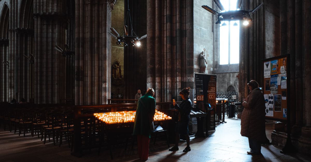 A person kneeling on a stone floor in a dark church, hands open, soft light from a stained glass window
