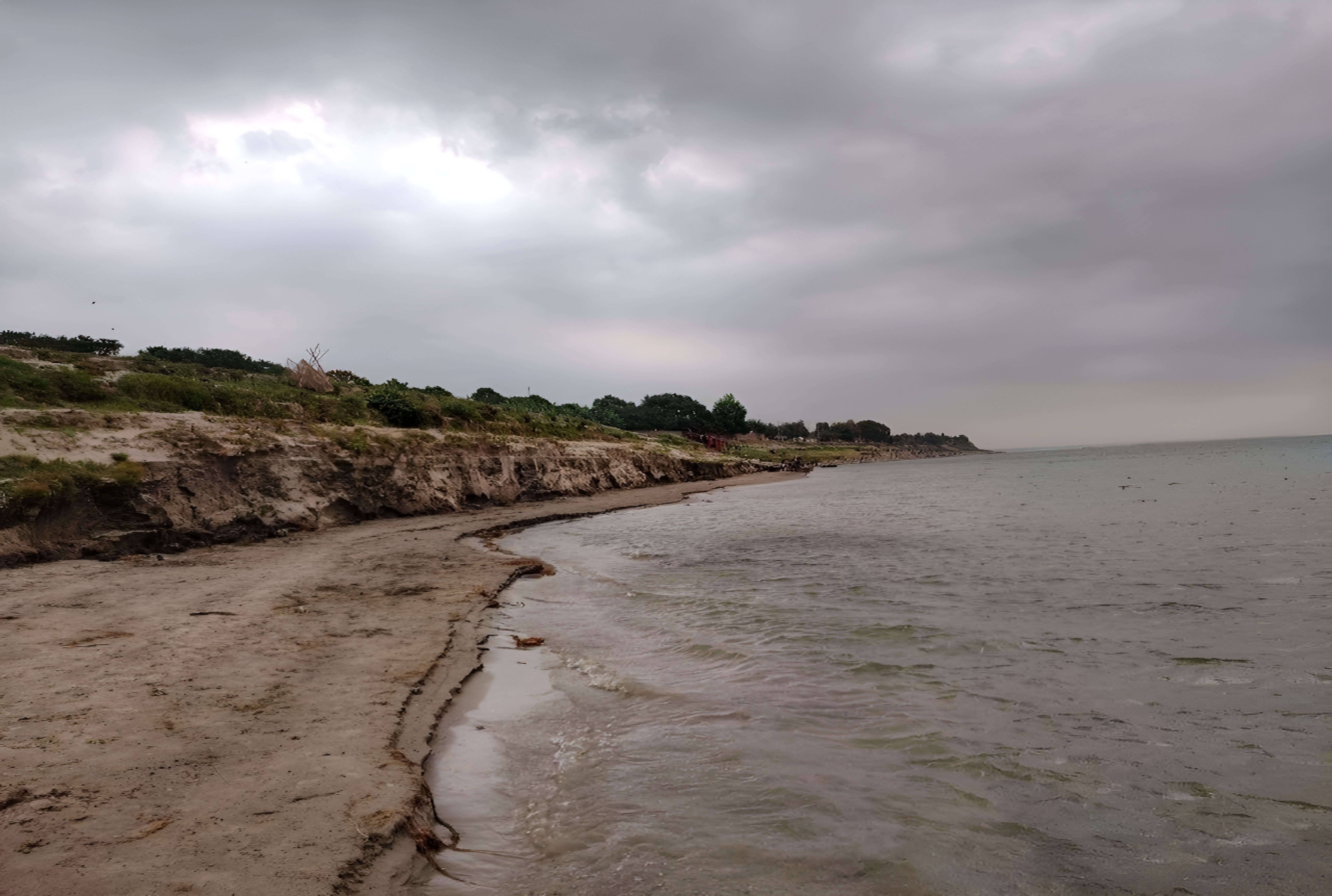 Una orilla oceánica gris y desierta bajo un cielo nublado.