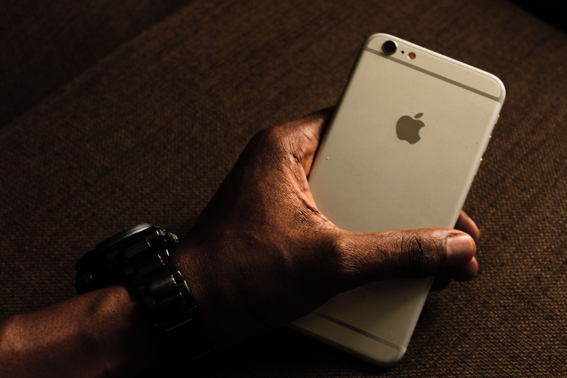 Stop Shaky Footage When Shooting Handheld With Your Phone Close-up of a hand holding a smartphone, wearing a wristwatch. Dark background setting.