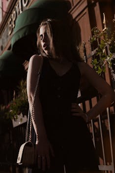 一位穿着连身裤的优雅女人在户外以戏剧性的姿势倚靠建筑背景