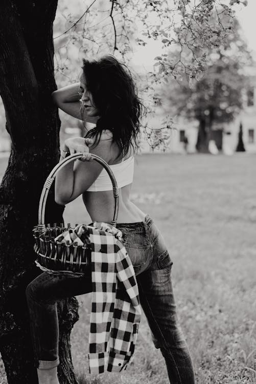 Free Grayscale Photo of Woman Carrying Basket While Leaning on Tree Posing Stock Photo