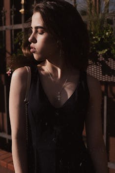 一位年轻女子身穿黑色连衣裙，在日落背景下闭着眼睛，陷入沉思