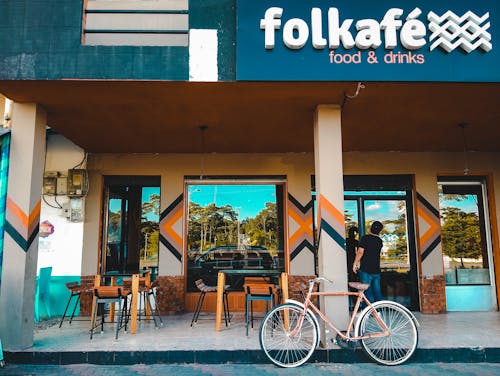 Brown Fixie Bike Near Concrete Wall and Two Person Standing on Closed Door About to Enter Inside Building