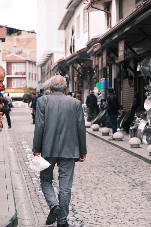 Free Elderly man in a gray suit walking through a bustling city street with traditional buildings. Stock Photo