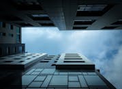 从低角度仰望多云天空下的现代摩天大楼，展现城市建筑设计