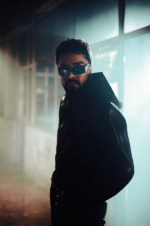 Free Stylish portrait of a man wearing sunglasses and a black leather jacket in a moody, backlit setting. Stock Photo