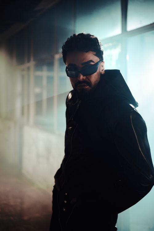 Free A man in a dark leather jacket and sunglasses poses in atmospheric lighting indoors. Stock Photo