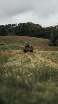 A tractor working in a lush, hilly countryside field under cloudy skies.