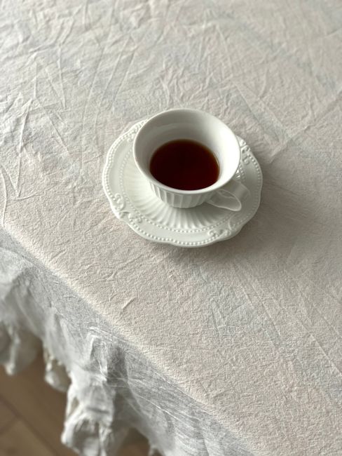 White teacup with dark tea on a textured white tablecloth, creating a minimalist and elegant scene.