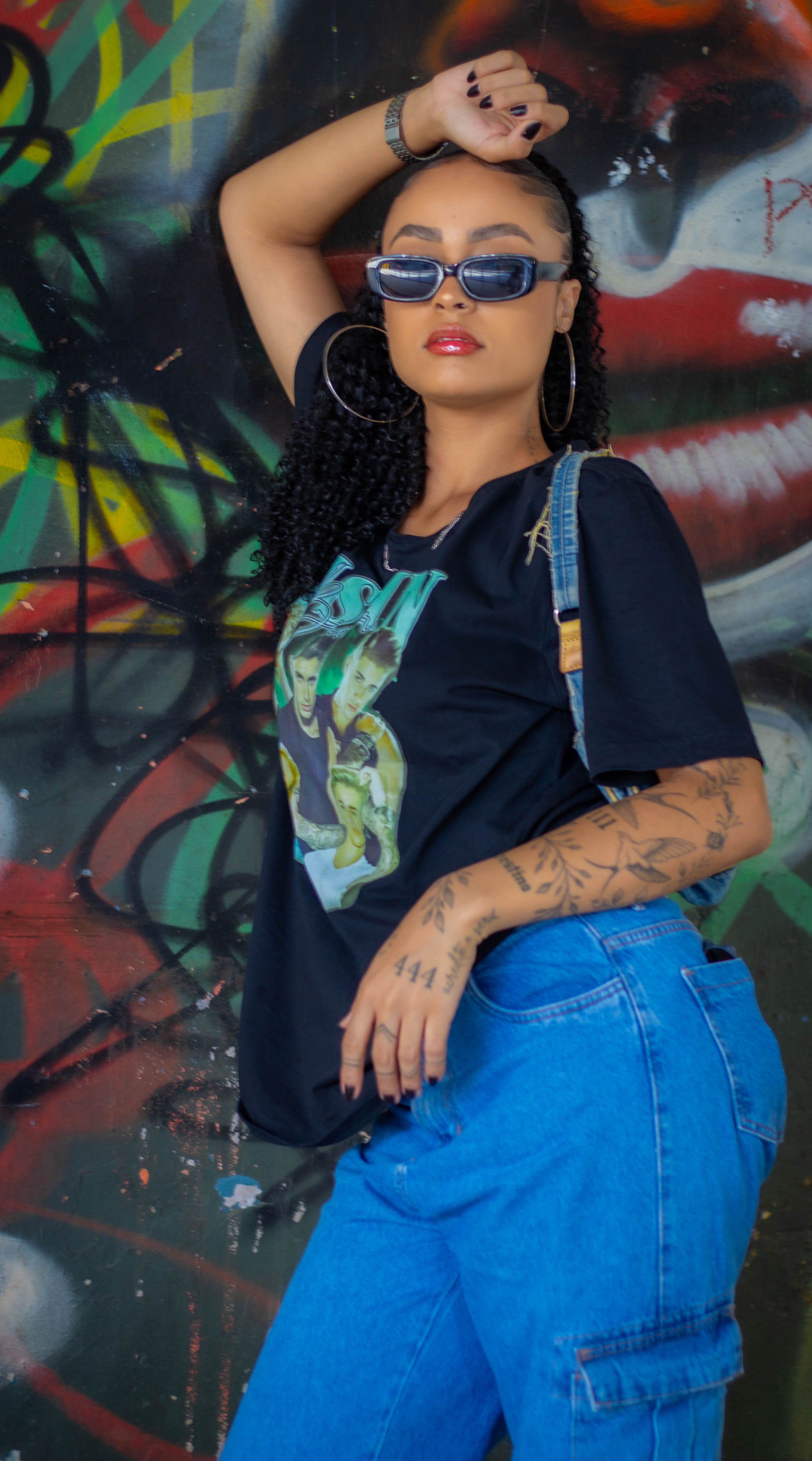 Mulher fashionista em pé contra uma parede de grafite vibrante, usando óculos escuros.