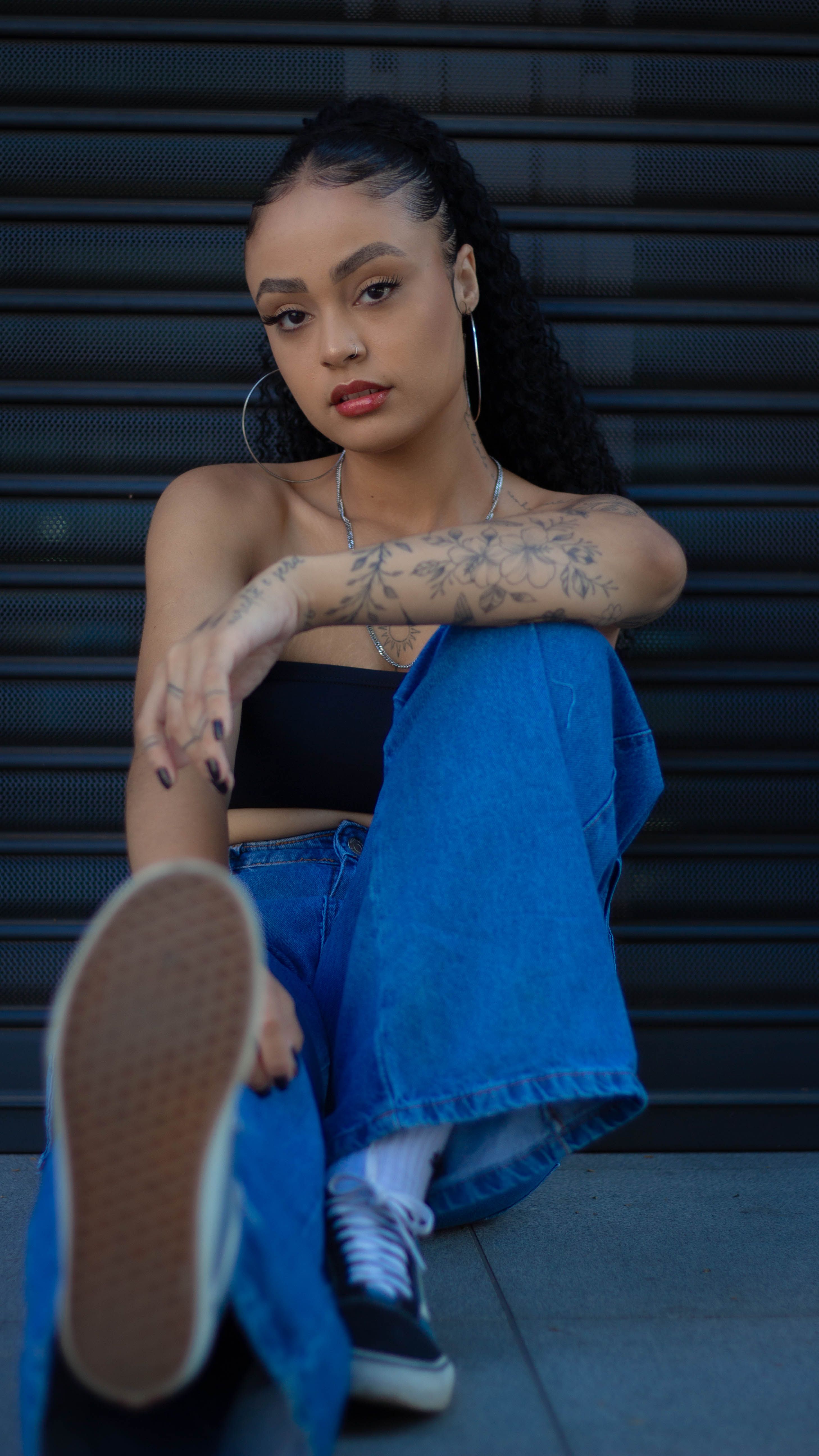 Fashionable woman with tattoos posing in jeans against a sleek urban wall. Youthful and edgy portrait.