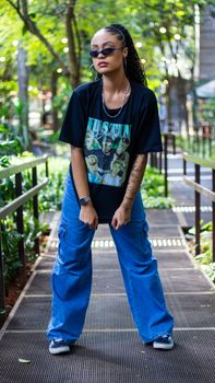 Stylish woman in sunglasses and relaxed attire posing in an urban outdoor setting.