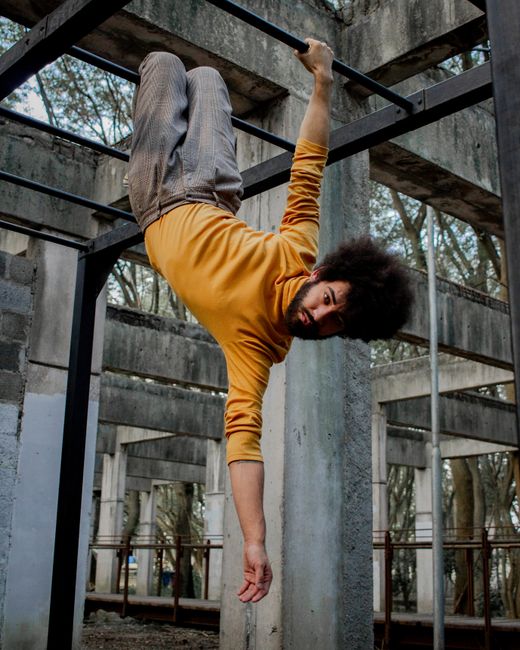 Man in yellow sweater hanging upside down in an industrial, outdoor setting.