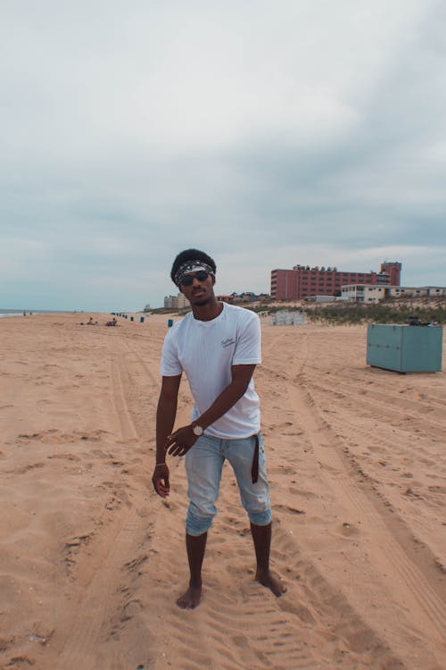 Homem De Camiseta Branca E Calça Jeans Em Pé Na Areia