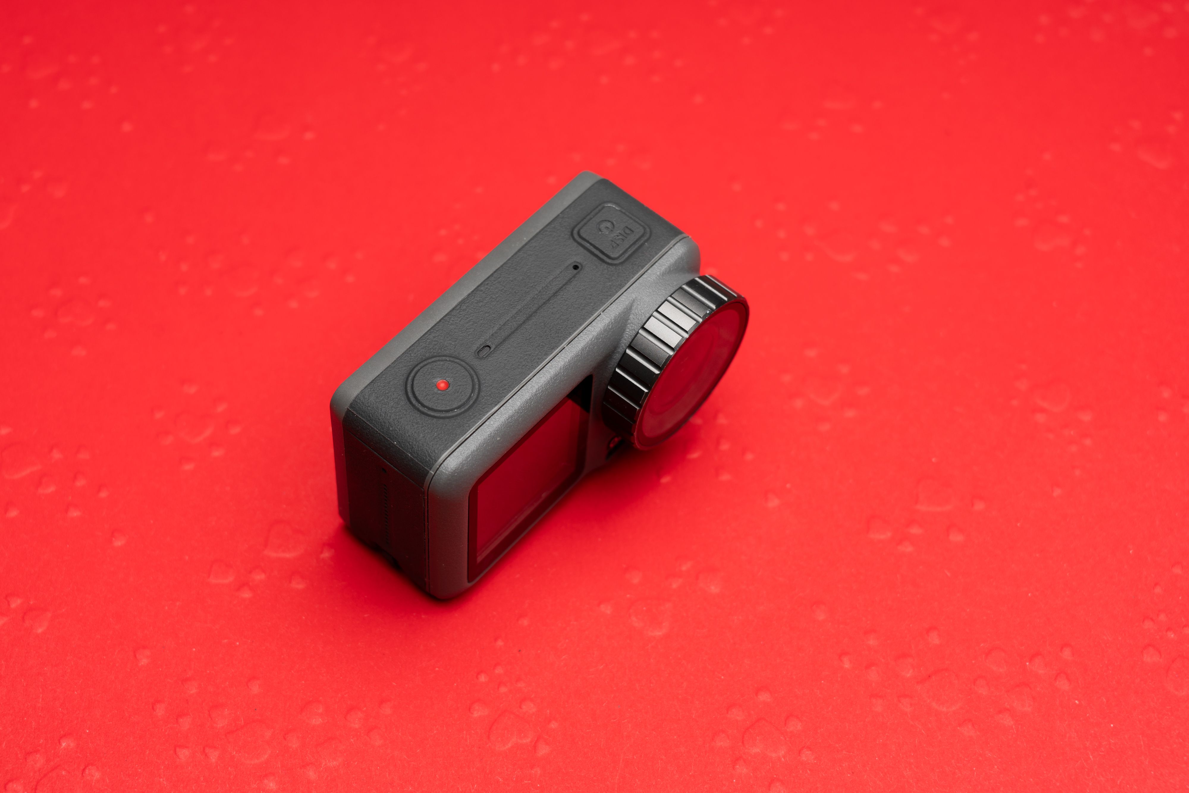 Gray action camera placed on a vivid red backdrop, showcasing its compact design and advanced features.