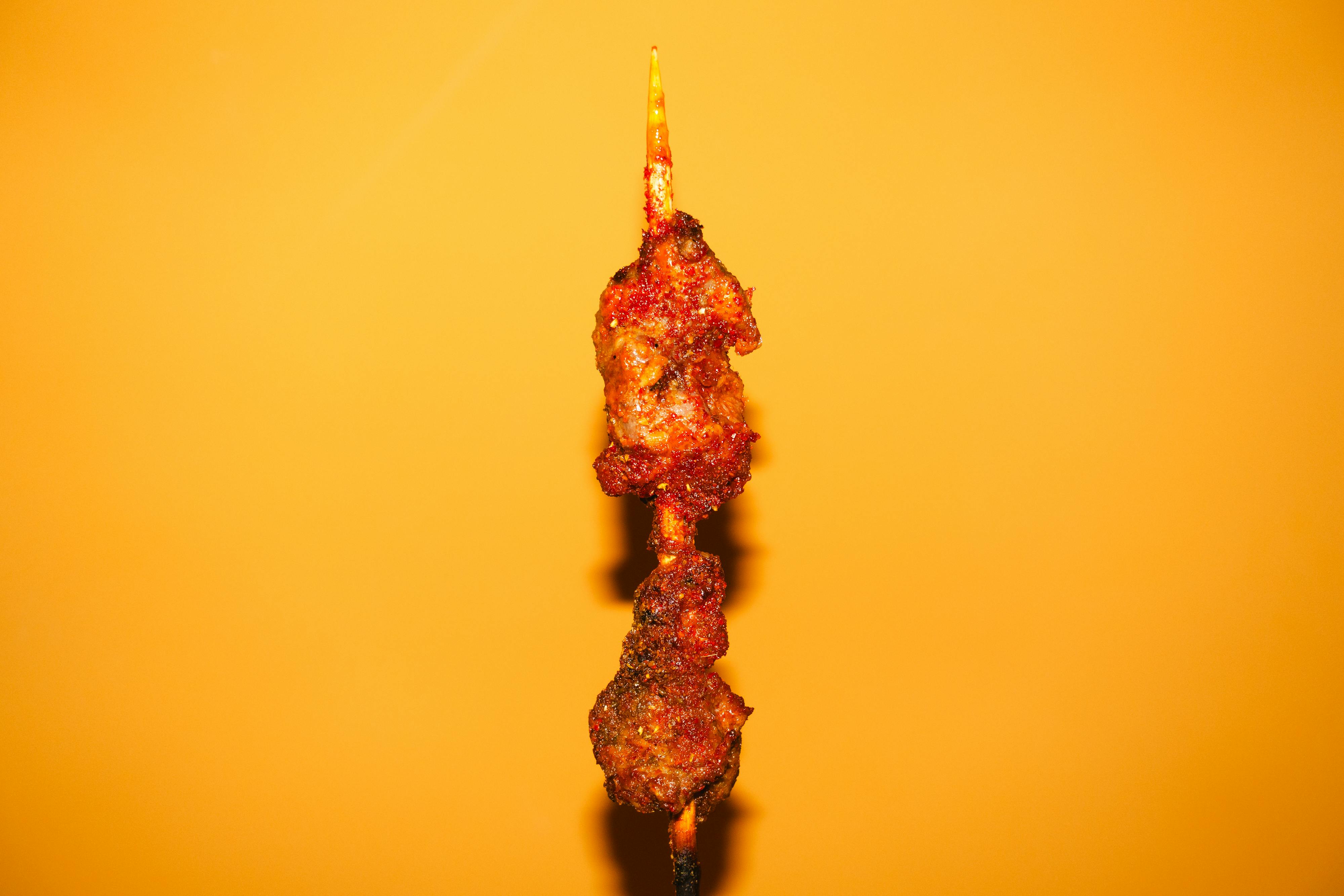 A skewer of meat on a stick with a yellow background · Free Stock Photo