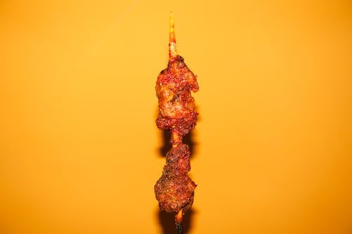 A skewer of meat on a stick with a yellow background