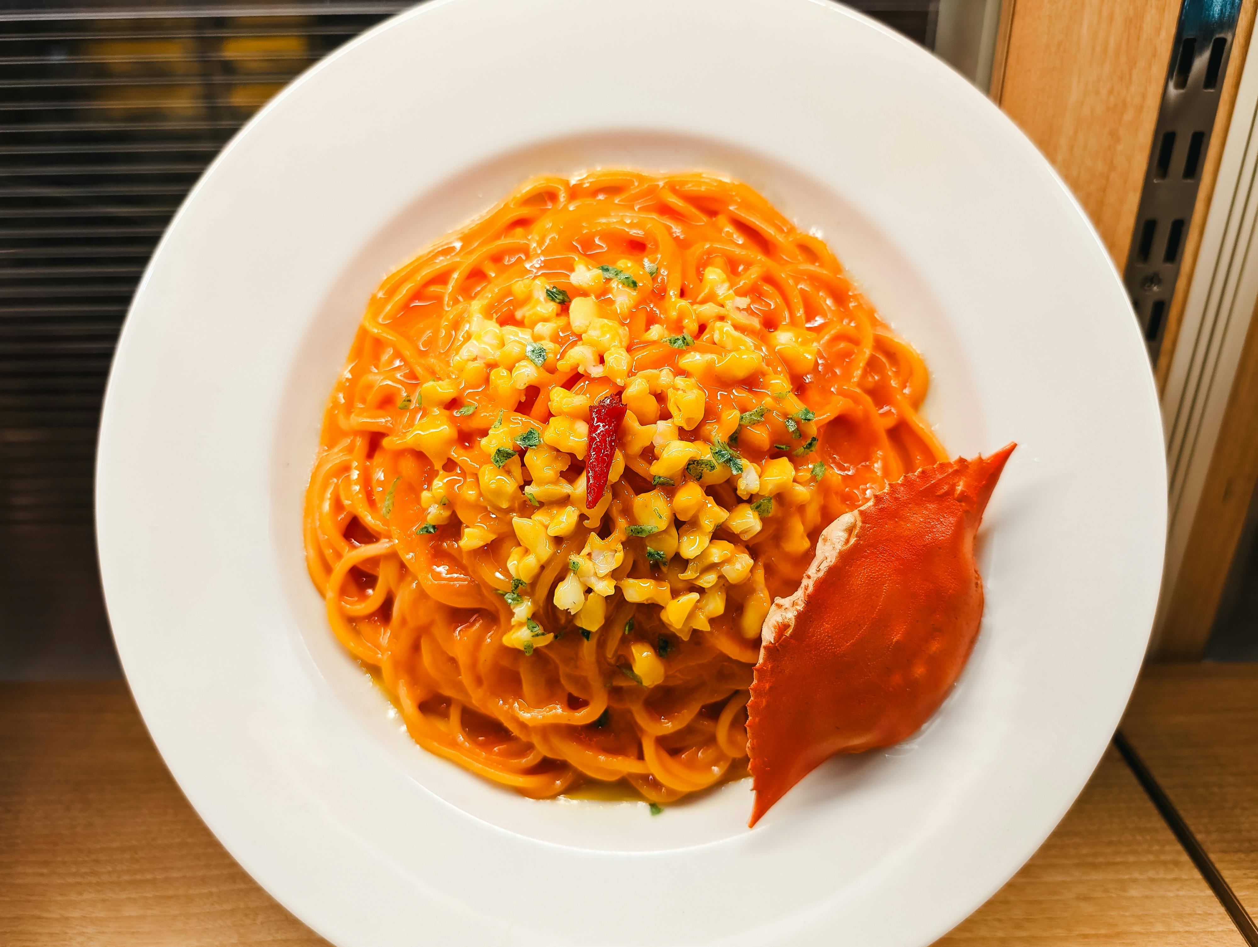 Plate of vibrant seafood pasta topped with sweetcorn and crab in a cozy setting.