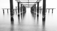 这张黑白照片宁静地展现了一个海洋码头，反光的海水和坚固的柱子清晰可见