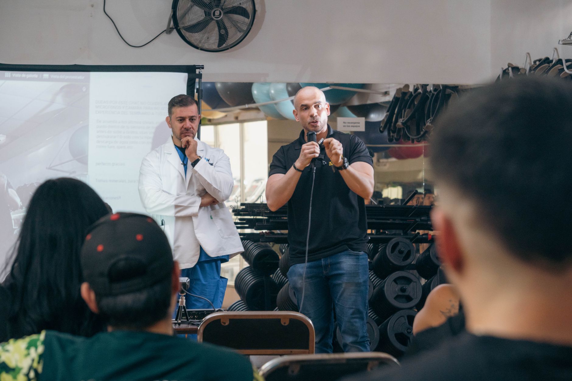 A doctor and fitness trainer conducting a seminar in a gym setting.